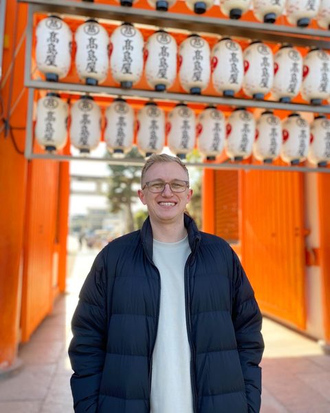 Hayden Schuster smiling under two rows of white paper lanterns on an orange gate