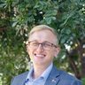 Hayden Schuster, smiling, in glasses and a blue blazer
